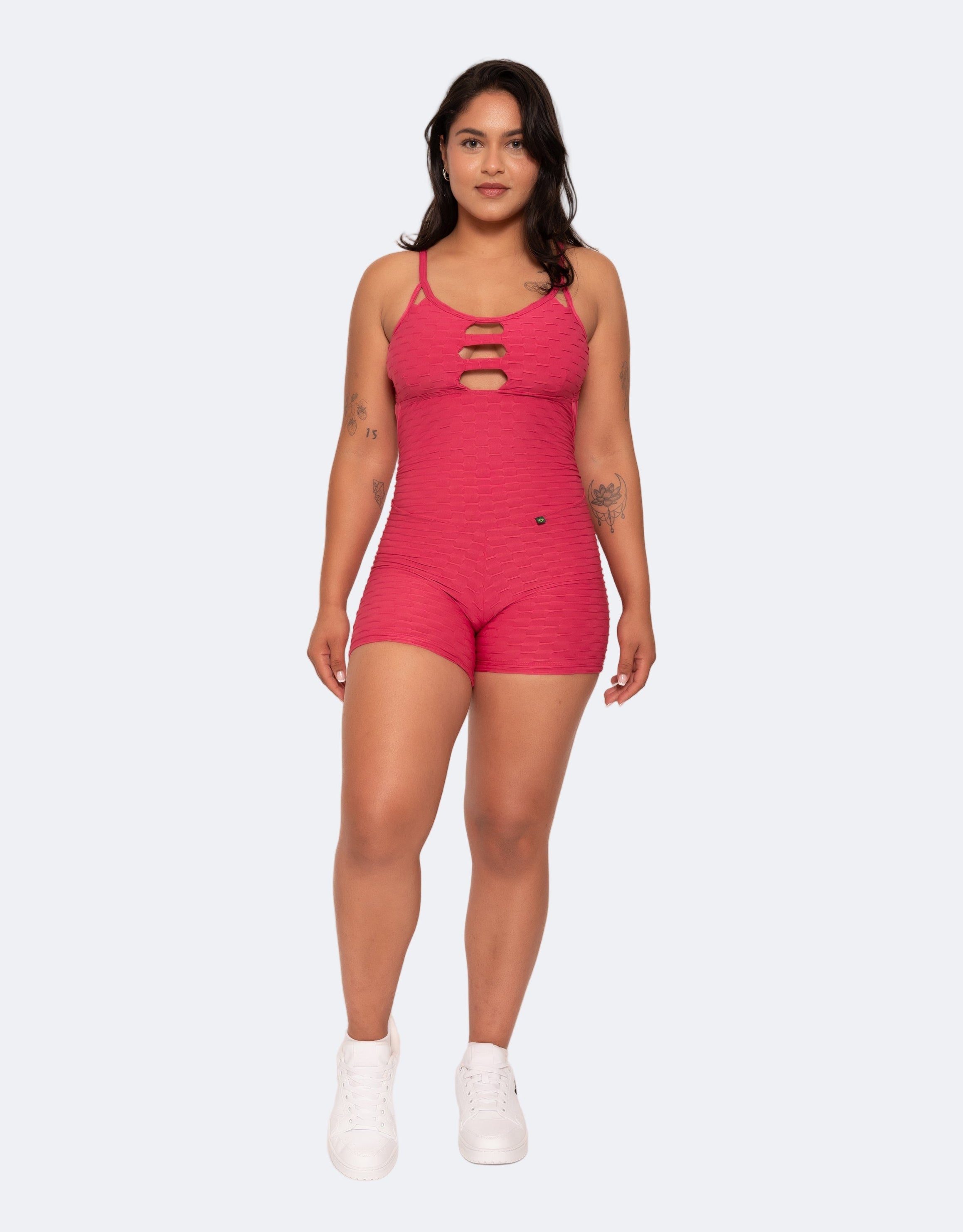 Female model wearing the Amelia Pink Short Brazilian Jumpsuit with V-neckline and cross-back straps, standing front-facing.