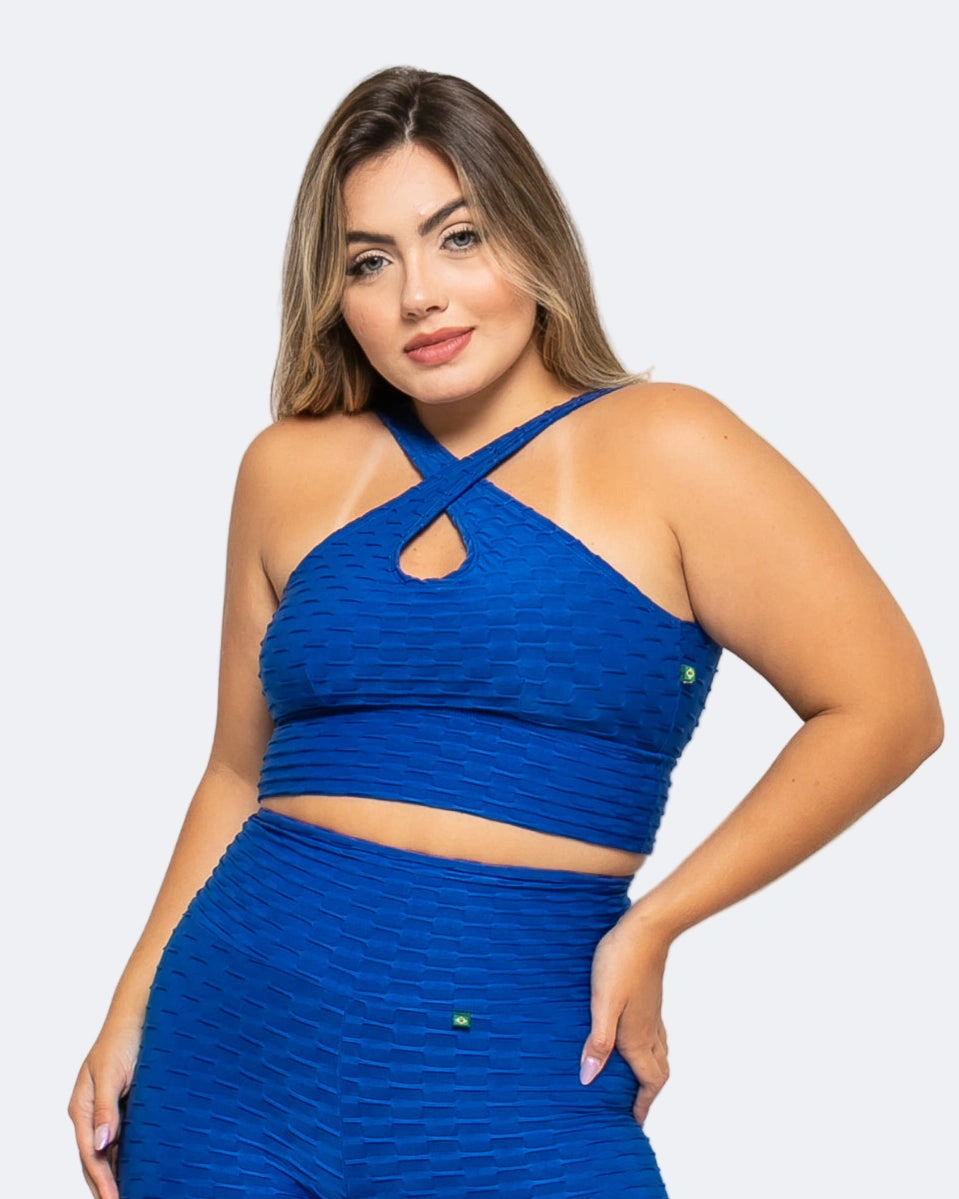 A woman wearing a blue sports bra with a textured fabric, featuring a halter neck and crisscross strap design.