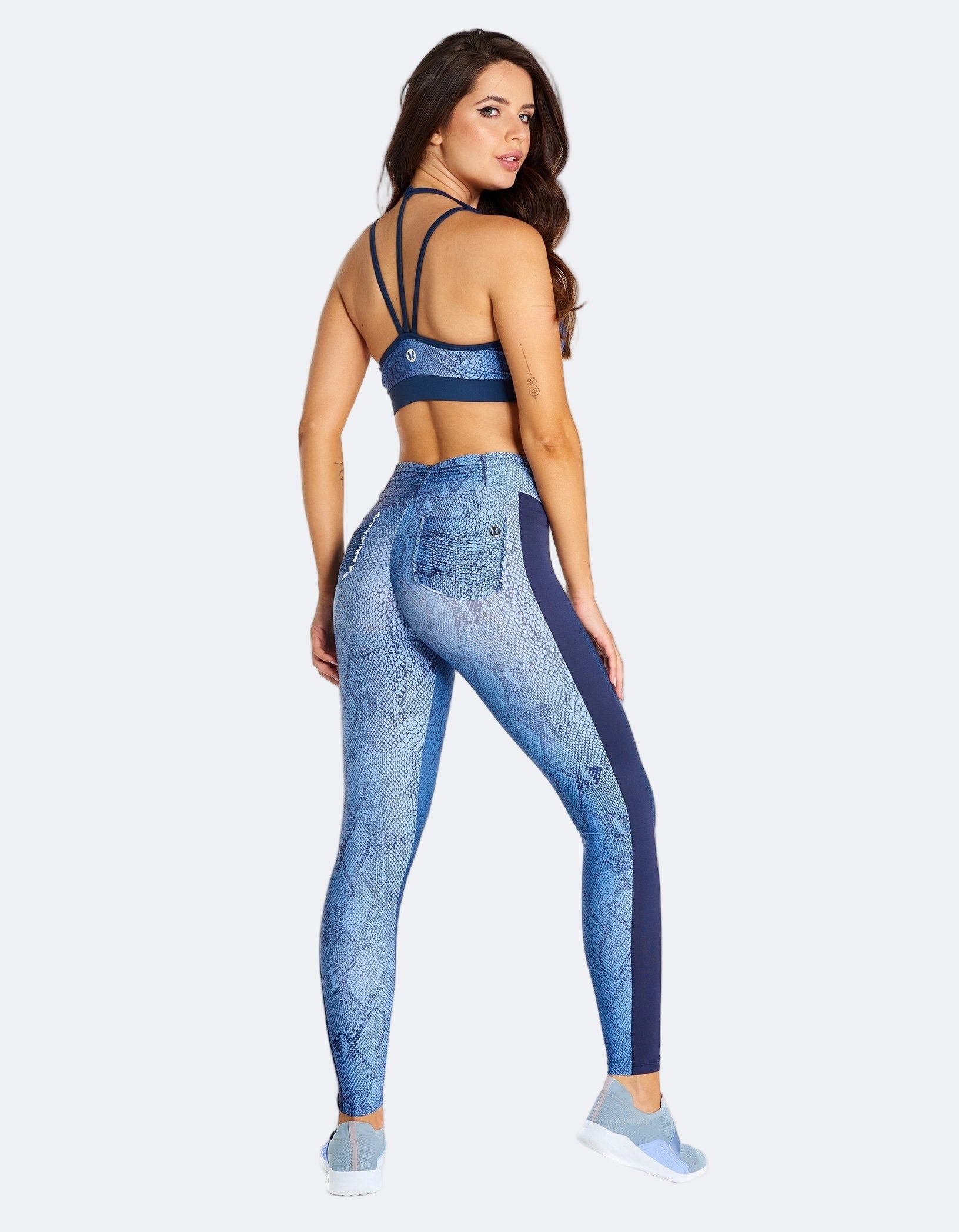 Woman wearing a blue snake print pattern sports bra and leggings on a cream background