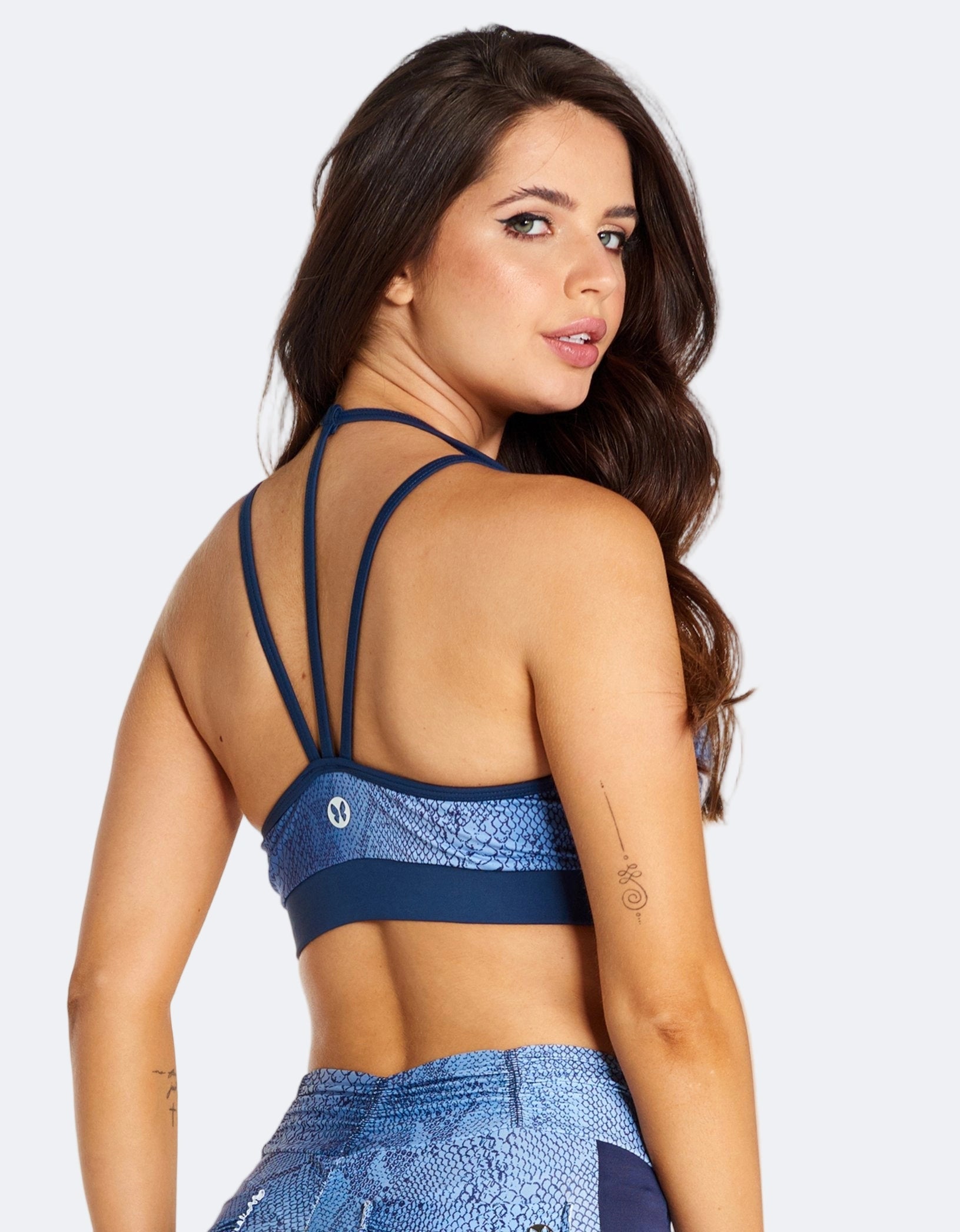 A sports bra with a blue snake print design, featuring a low cut front with a strappy design and removable padding.