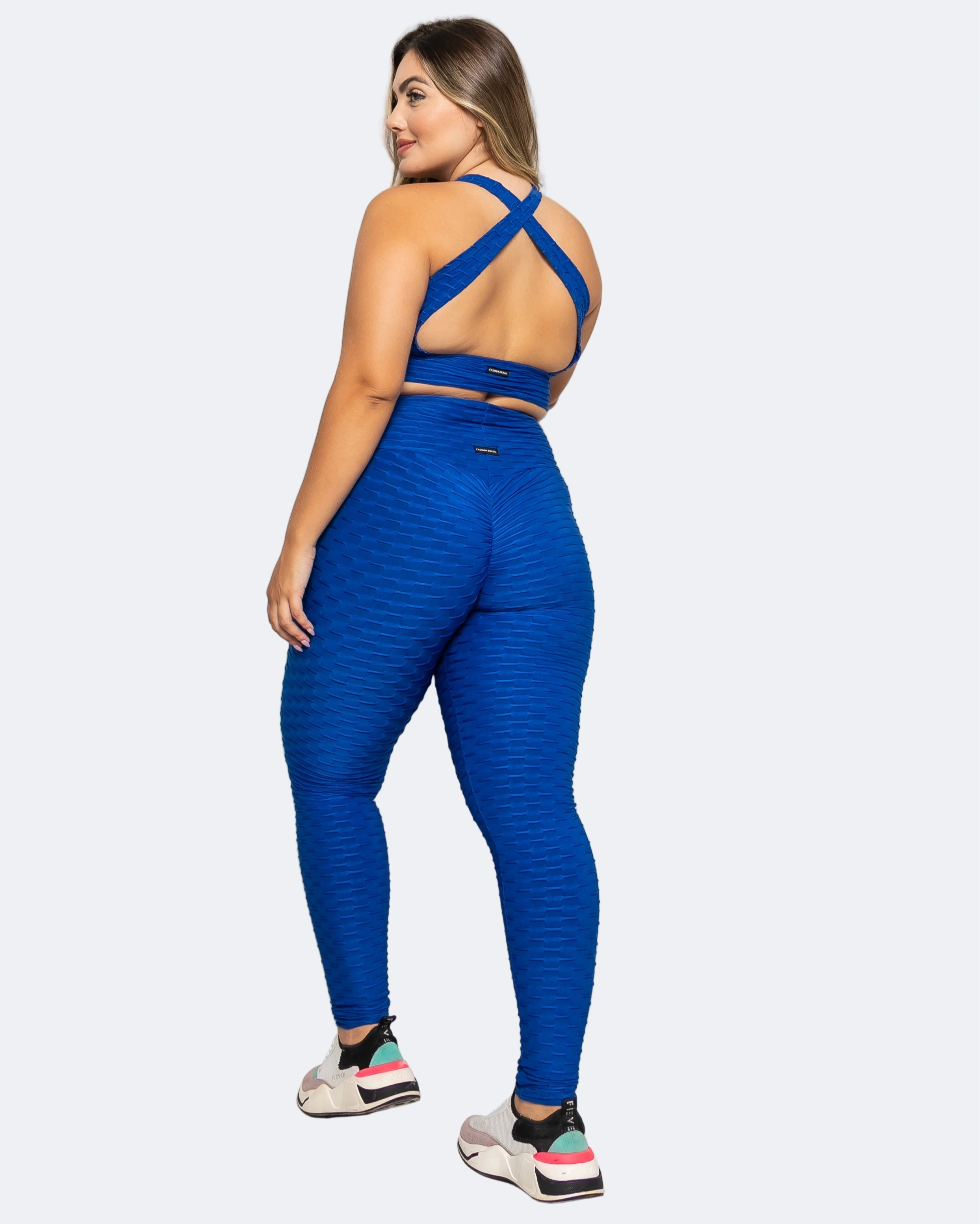 Woman wearing a blue athletic outfit with criss-cross back design on a white background