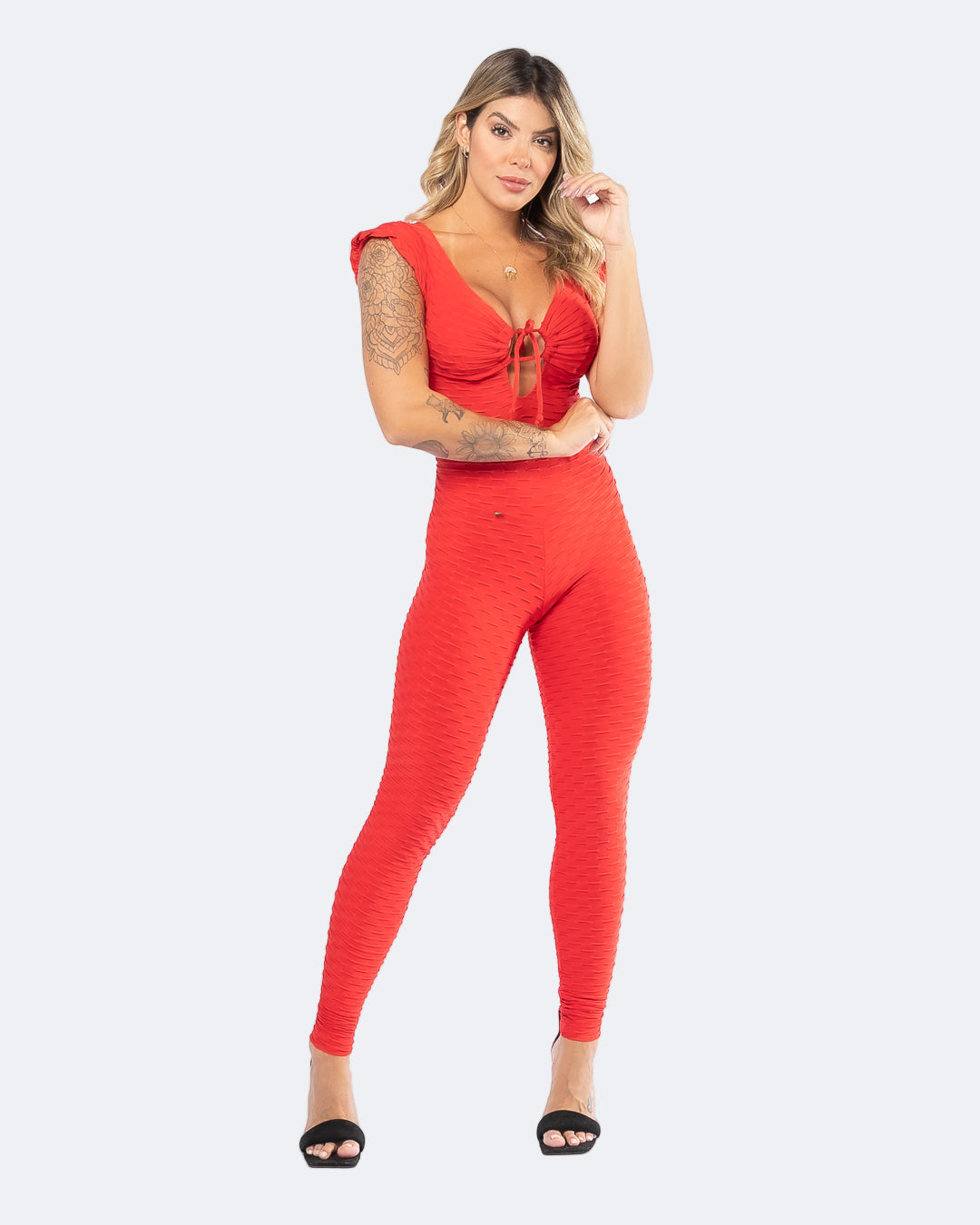A female model wearing a red sleeveless V-neck jumpsuit with short sleeves and an open back, posing against a white background.