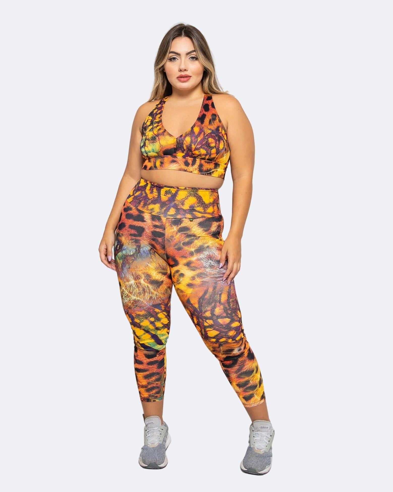Woman wearing a colorful safari animal print sports bra and leggings set on a white background.