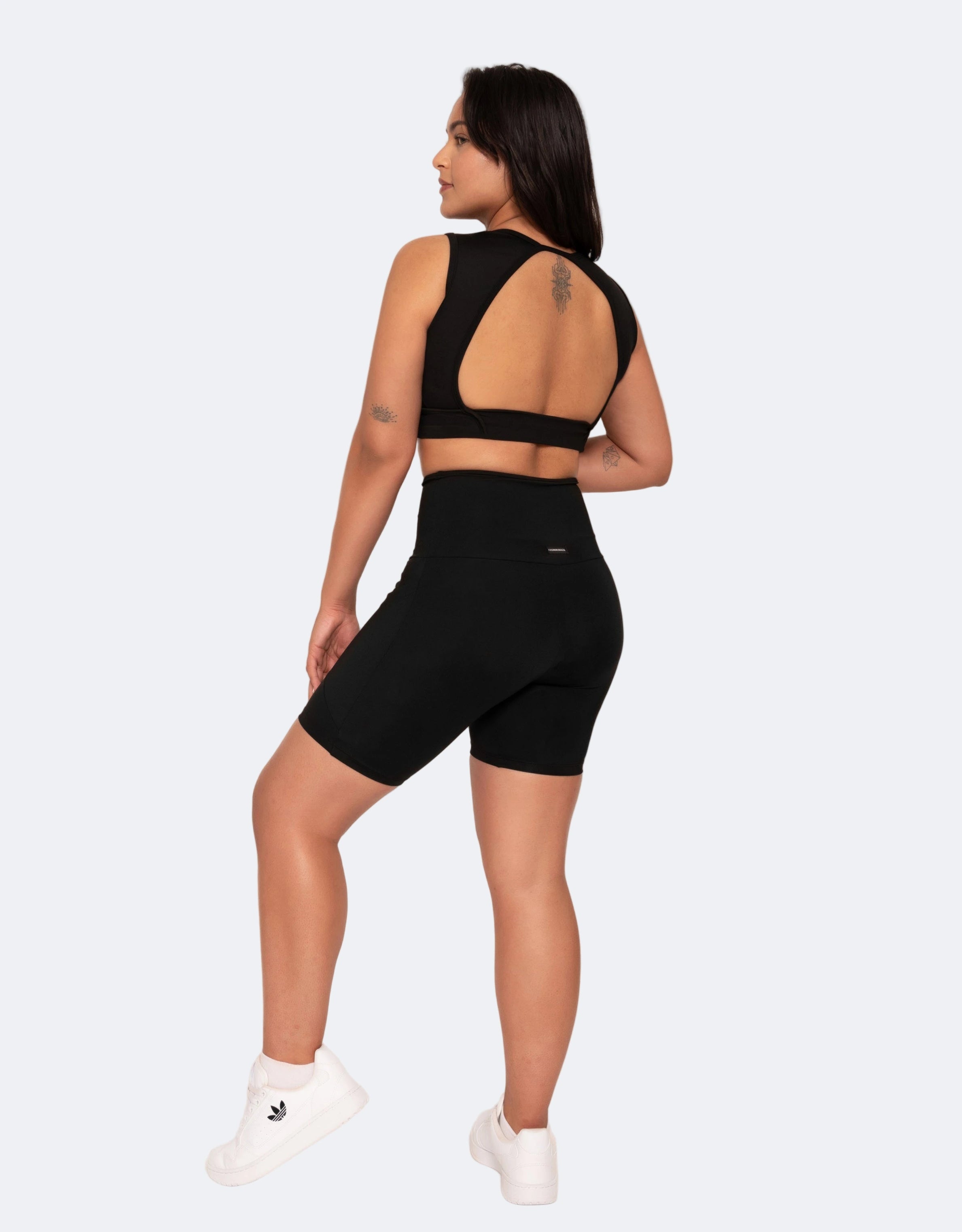 Back view of model is  wearing a black mid length high waisted shorts and black active crop top on a white background