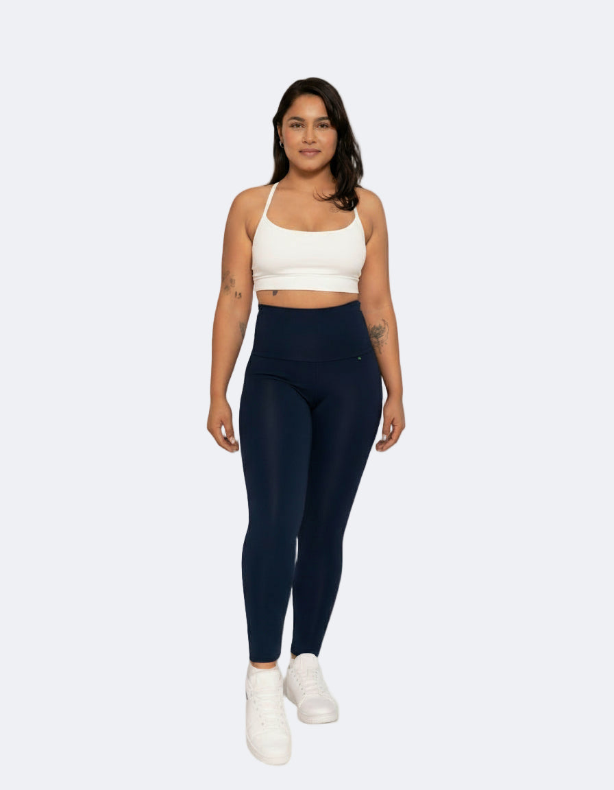 A model wearing navy high-rise compression leggings with a white top and white sneakers.