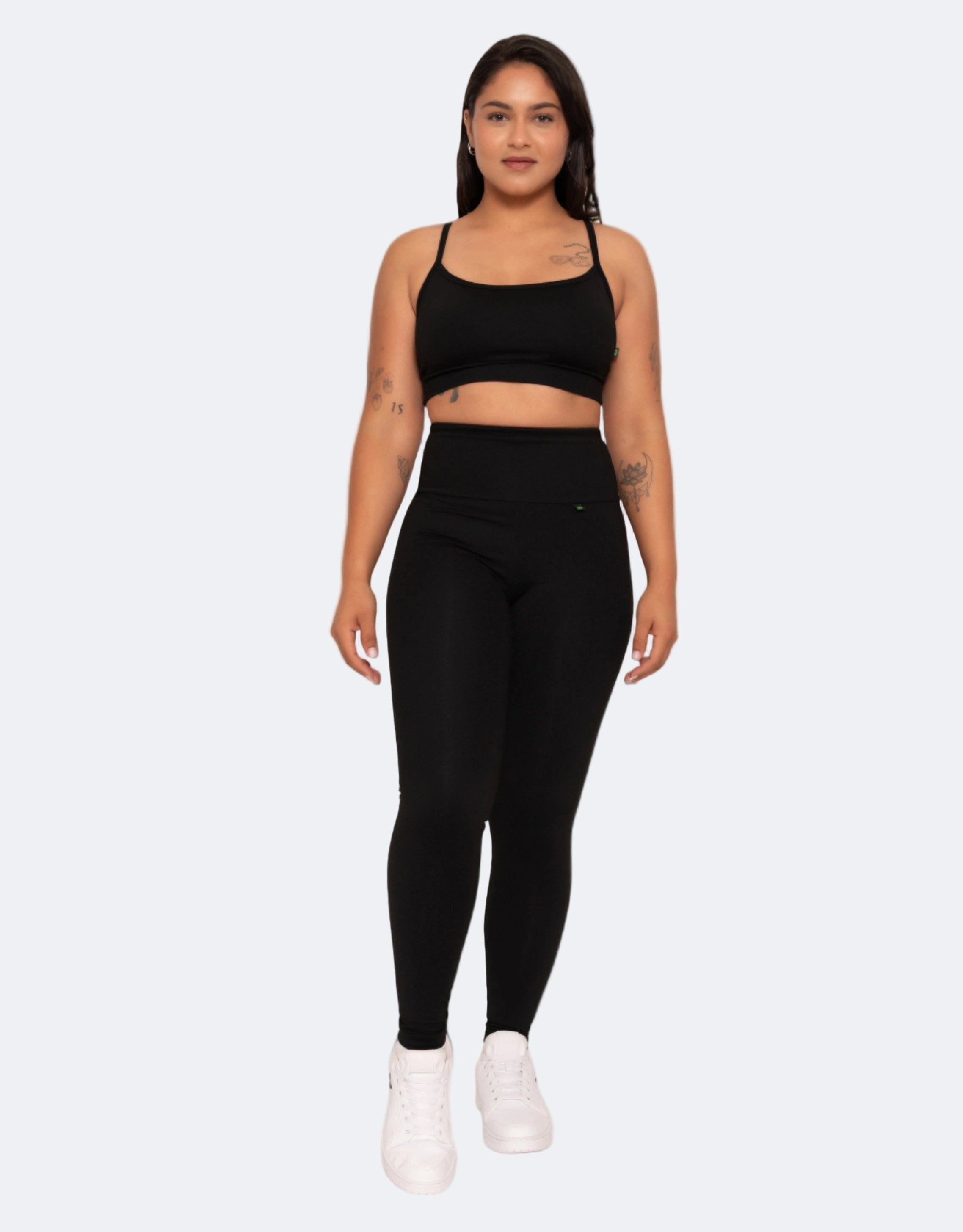 Model wears high compression black high waisted black leggings  and matching top on a white background