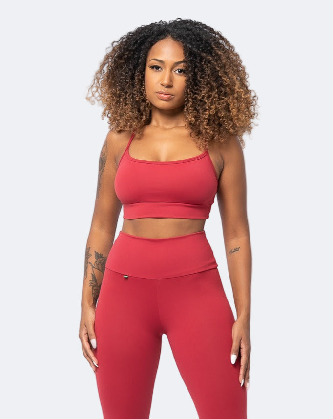 A female model wearing a red sports crop top and matching leggings with a cross-back design.