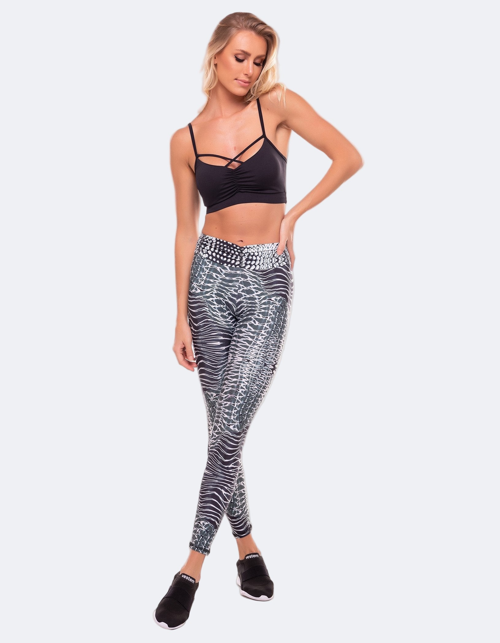 Woman wearing a black sports bra and patterned leggings on a white background