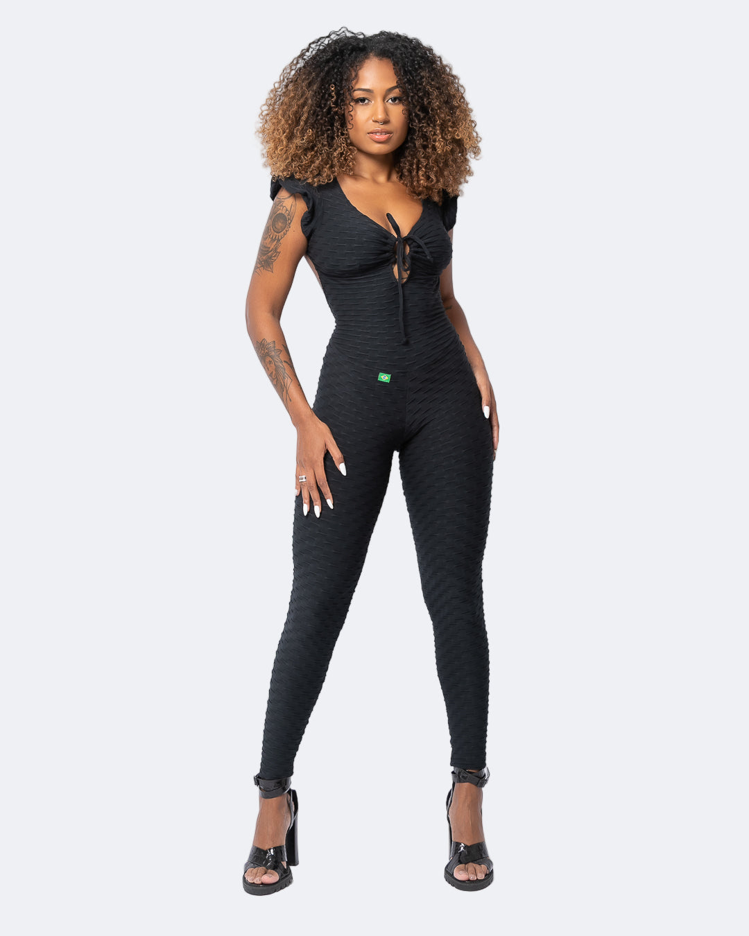 Model wearing Fashion Brazil black jumpsuit with short sleeves and an open back. The jumpsuit is full length and form-fitting. 